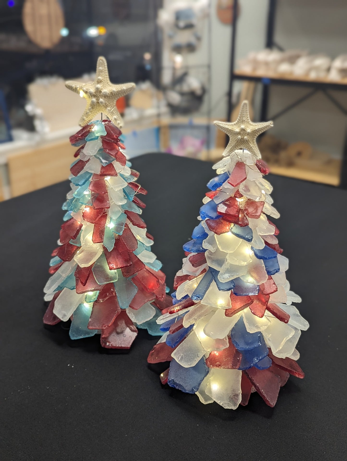 Two small, multicolored Christmas trees with star tops on a dark surface.