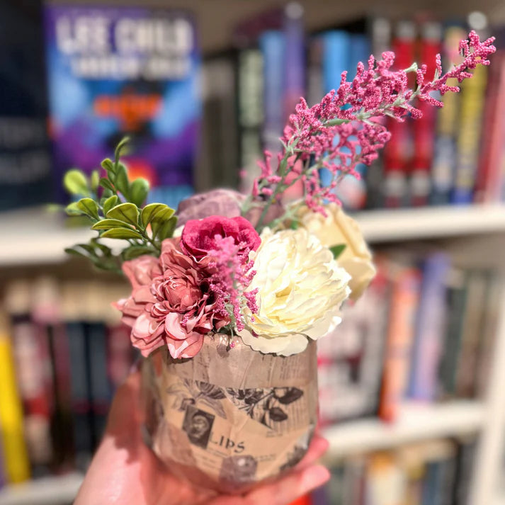 Small bouquet of flowers in a decorative vase held in front of a bookshelf.