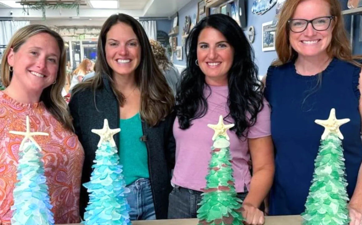 Four women standing behind a table with sea glass Christmas trees.