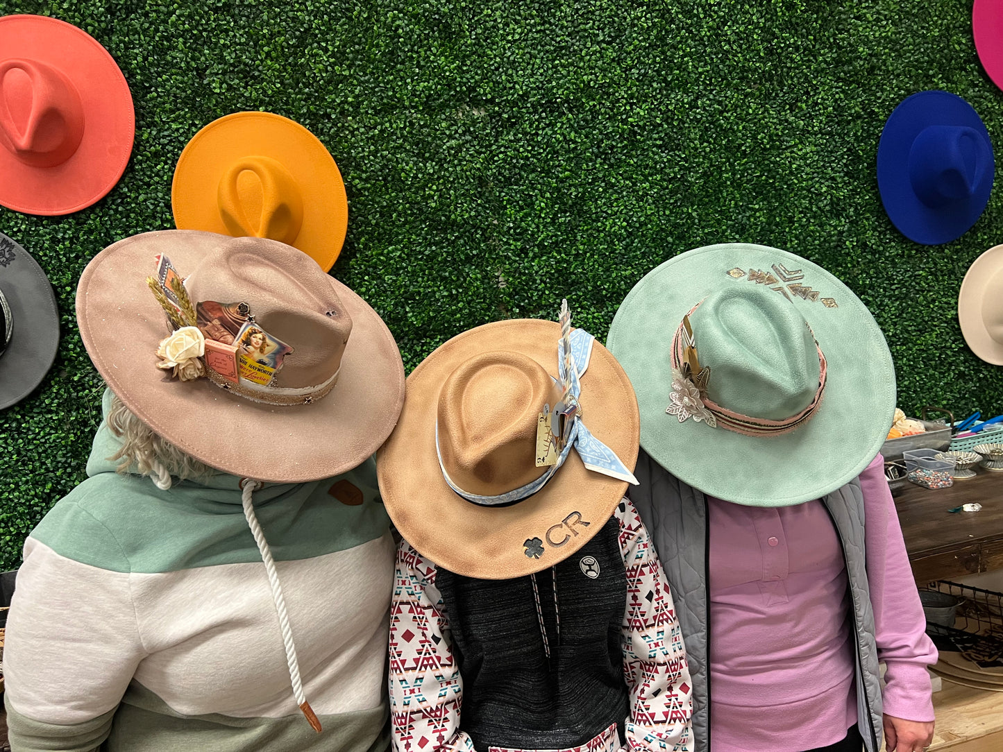 Three people wearing decorative hats with a grassy background