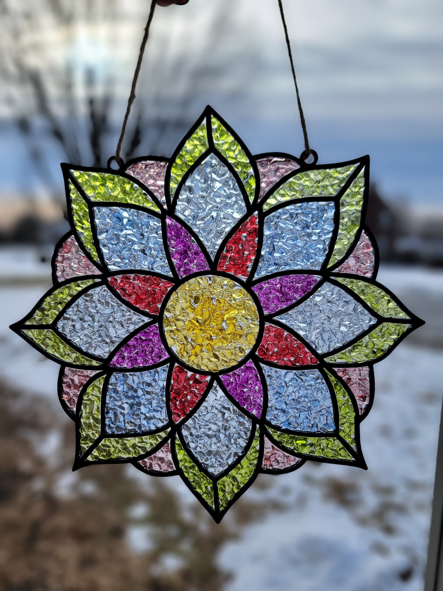 Colorful stained glass flower-shaped window hanging against a blurred outdoor background