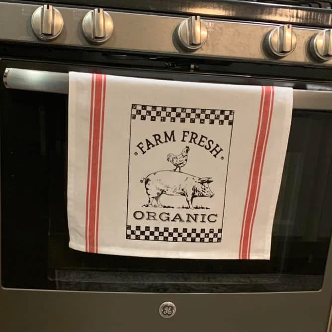 Tea towel with 'Farm Fresh Organic' text and graphics hanging on a stove handle.