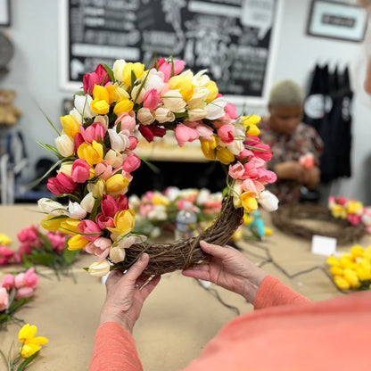 Person holding a floral wreath made of tulips in a workshop setting.