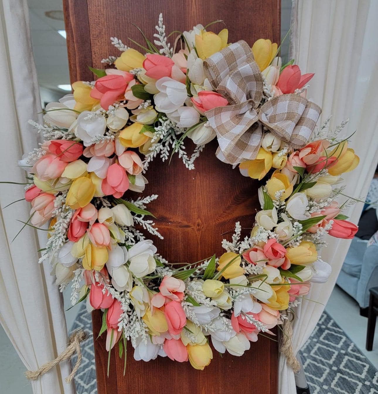 Floral wreath with colorful flowers and a checkered bow on a wooden door.