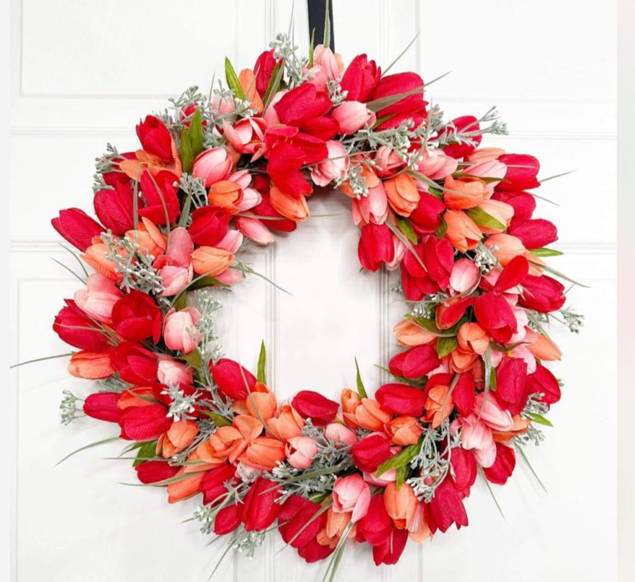 Floral wreath with red, pink, and orange tulips on a white door.