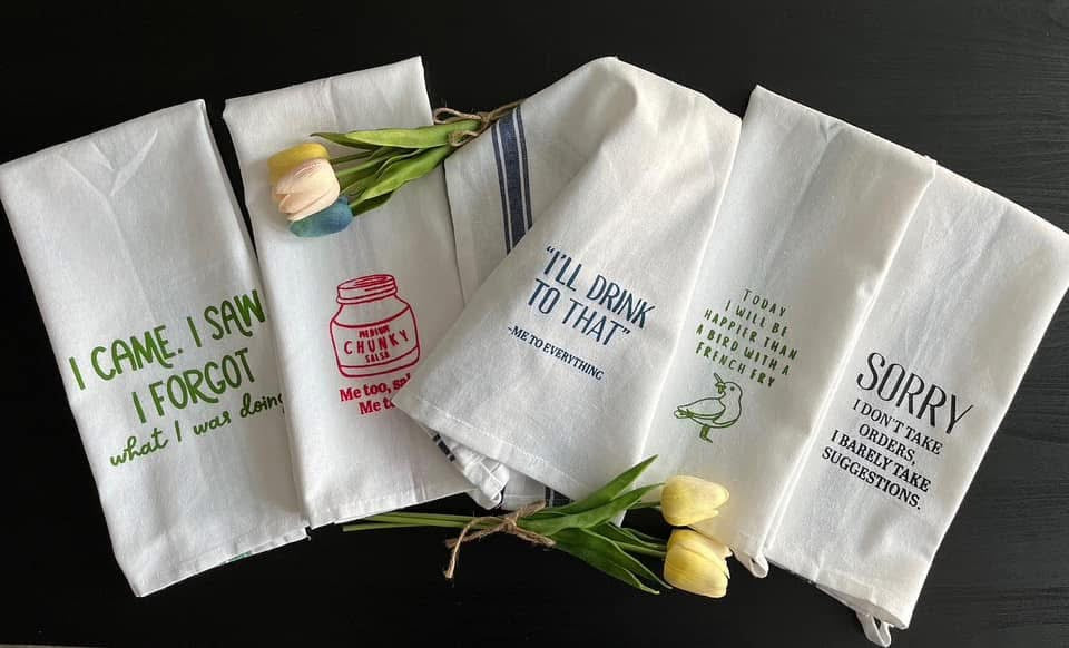 Set of four white towels with printed text and graphics on a dark surface.