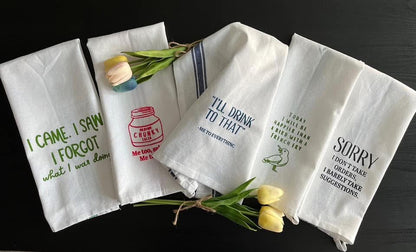 Set of four white towels with printed text and graphics on a dark surface.