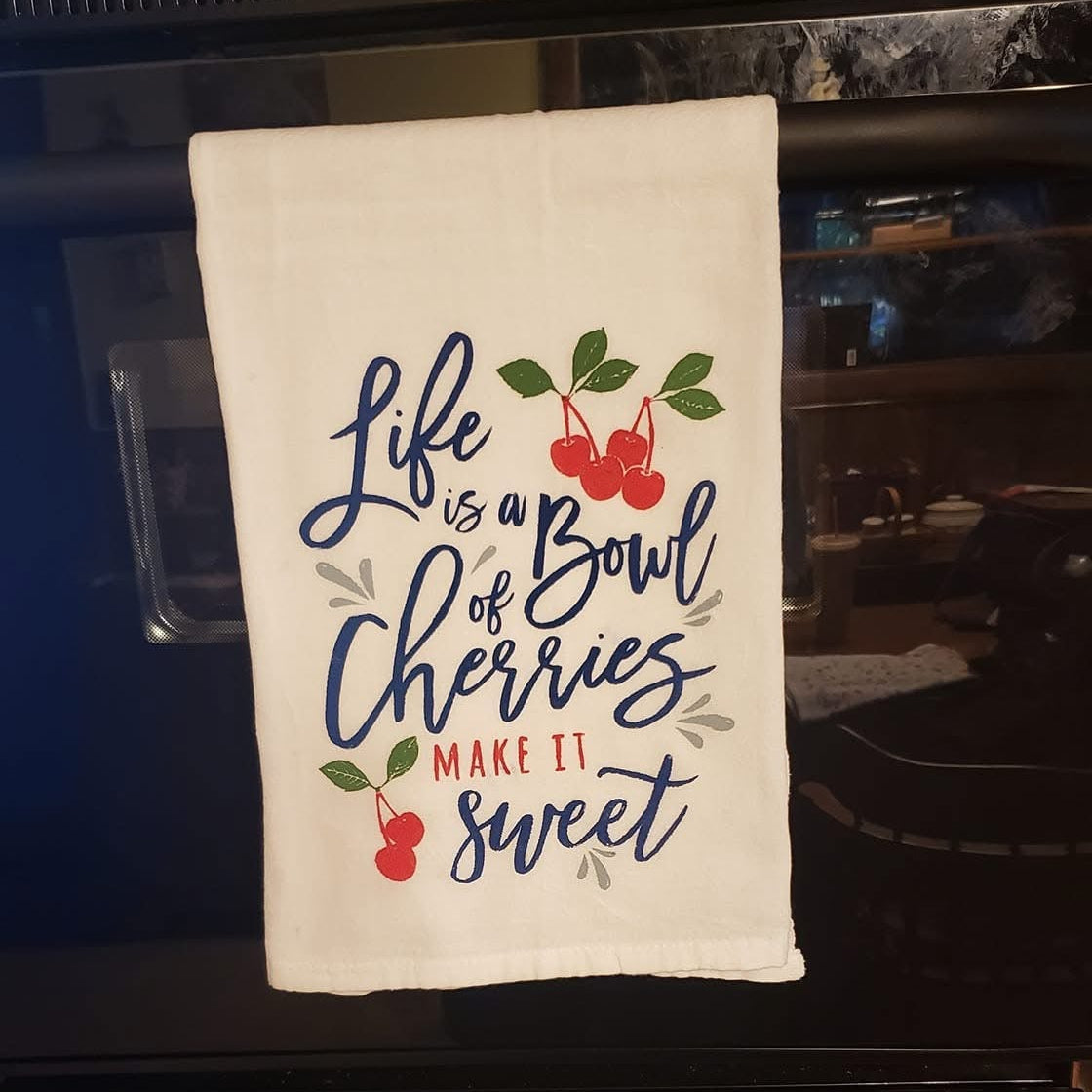 Decorative towel with 'Life is a Bowl of Cherries' text on an oven.