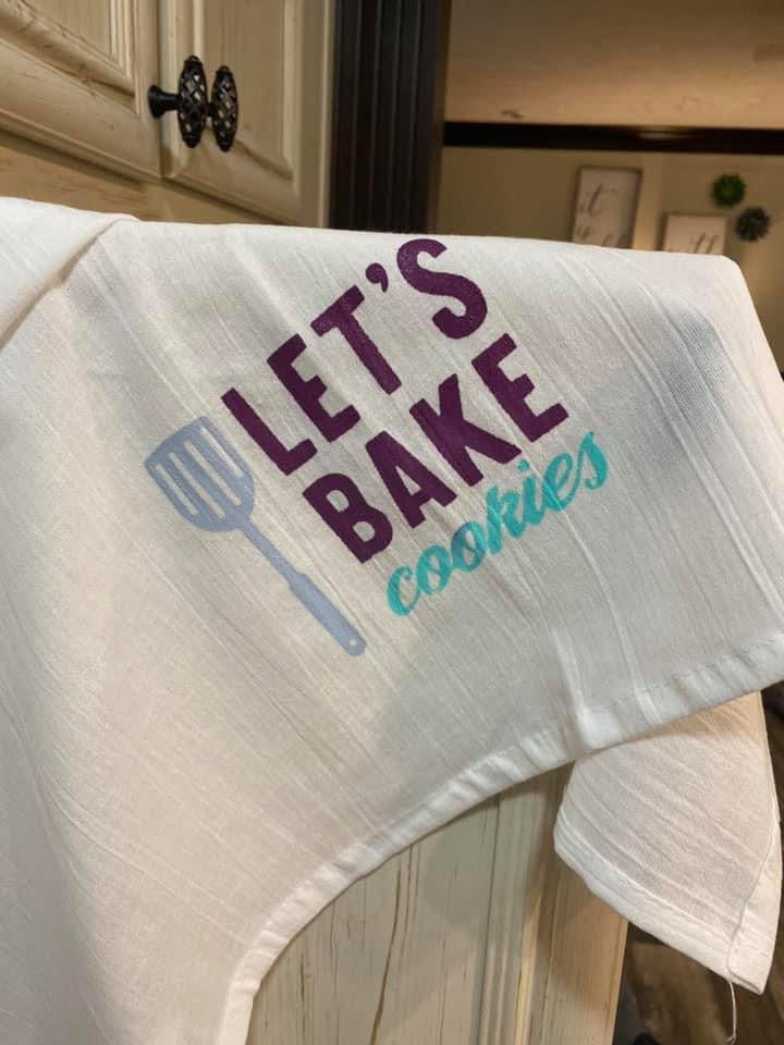White towel with 'Let's Bake Cookies' text and spatula graphic in a kitchen setting