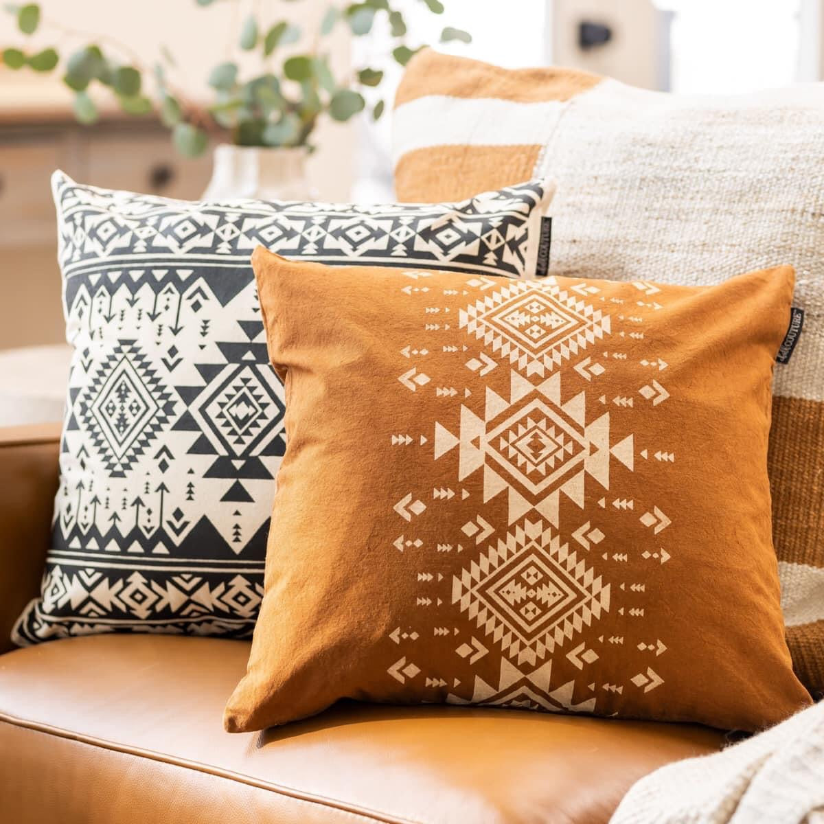 Two Aztec patterned pillows on a couch with a blurred indoor background