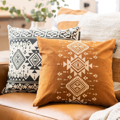 Two Aztec patterned pillows on a couch with a blurred indoor background