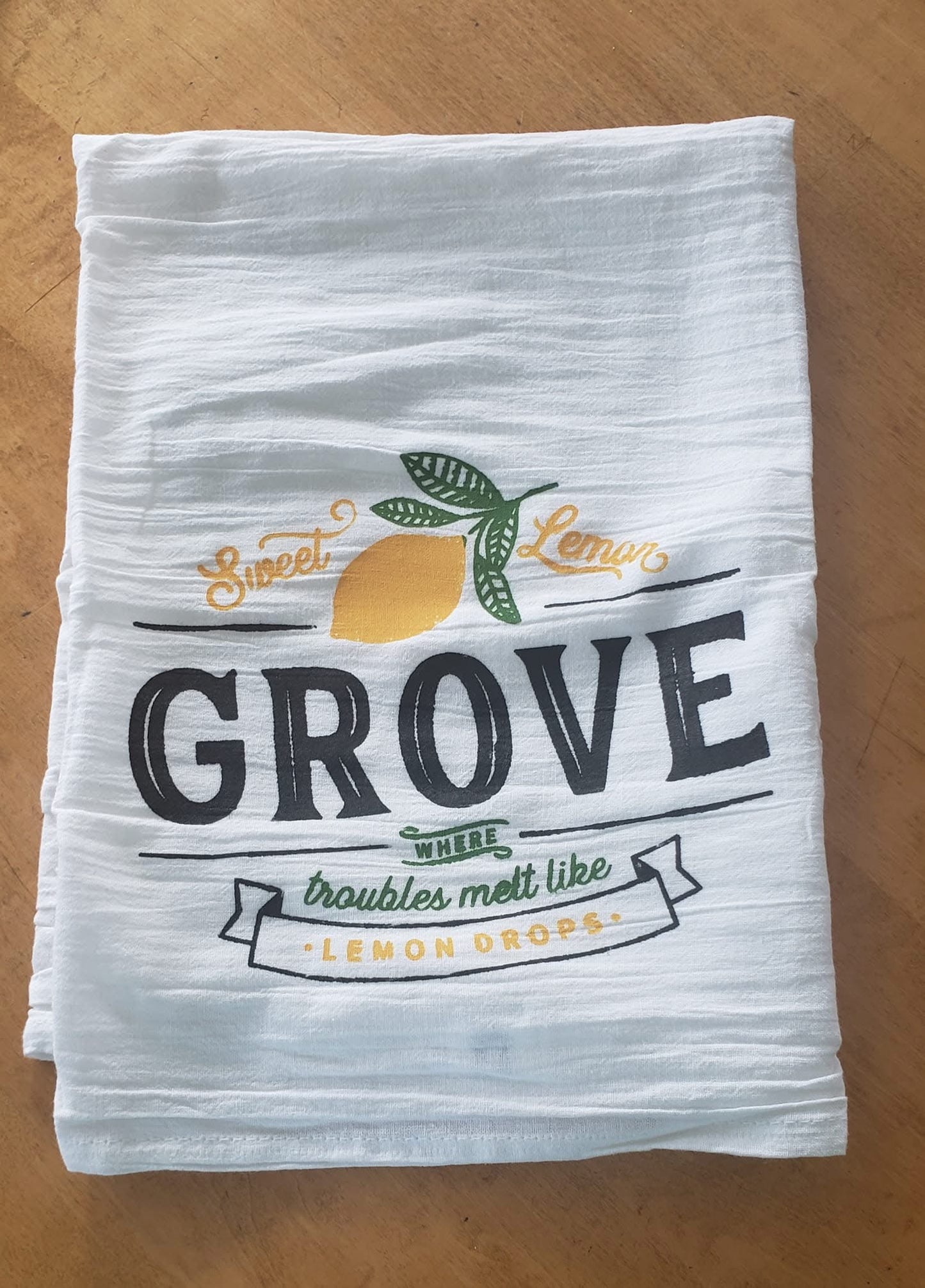 Stack of white towels with 'Sweet Lemon Grove' design on a wooden surface