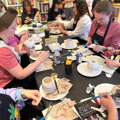 People sitting around a table with various items including cups, plates, and books in a casual setting.