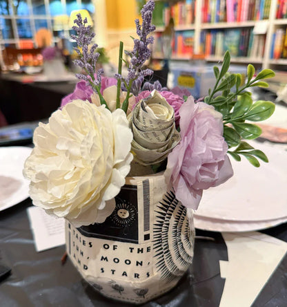 Floral arrangement in a decorative vase on a table with books in the background