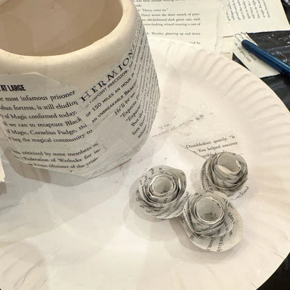Decorative paper cups made from newspaper with a roll of newspaper in the background.