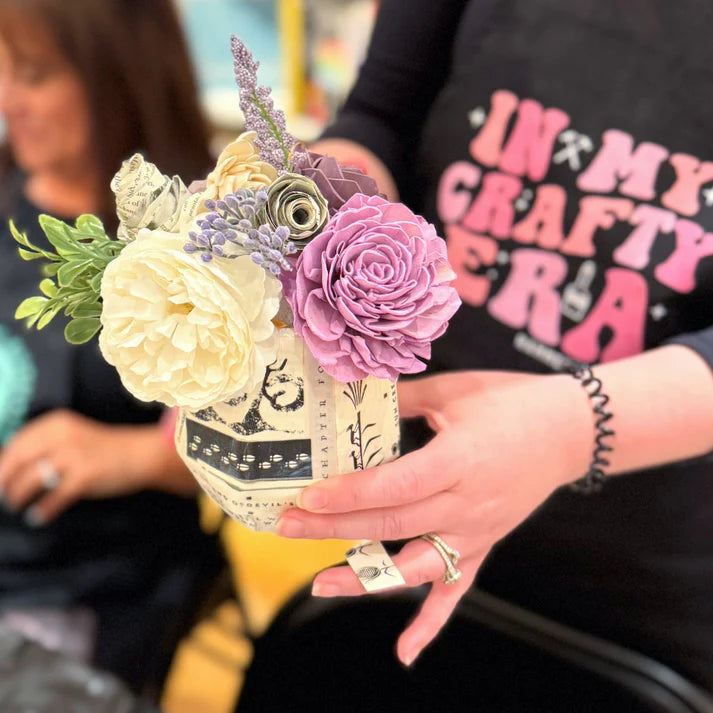 Person holding a bouquet of flowers in a decorative vase with a blurred background