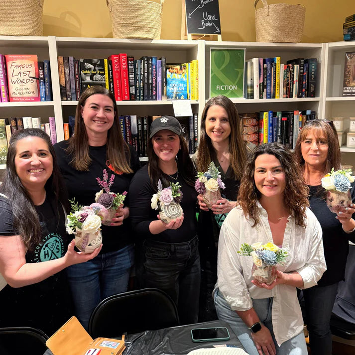 Group of women holding small floral arrangements in a room with bookshelves.