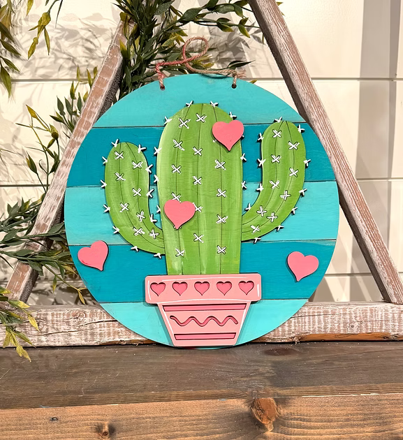 Decorative wall art with a cactus design on a wooden frame.
