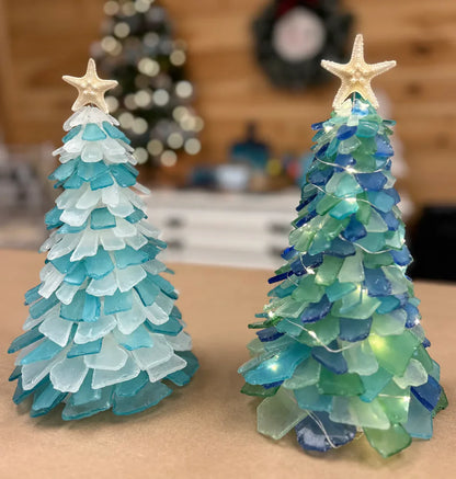 Two decorative Christmas trees made of sea glass with starfish on top, set against a blurred indoor background.