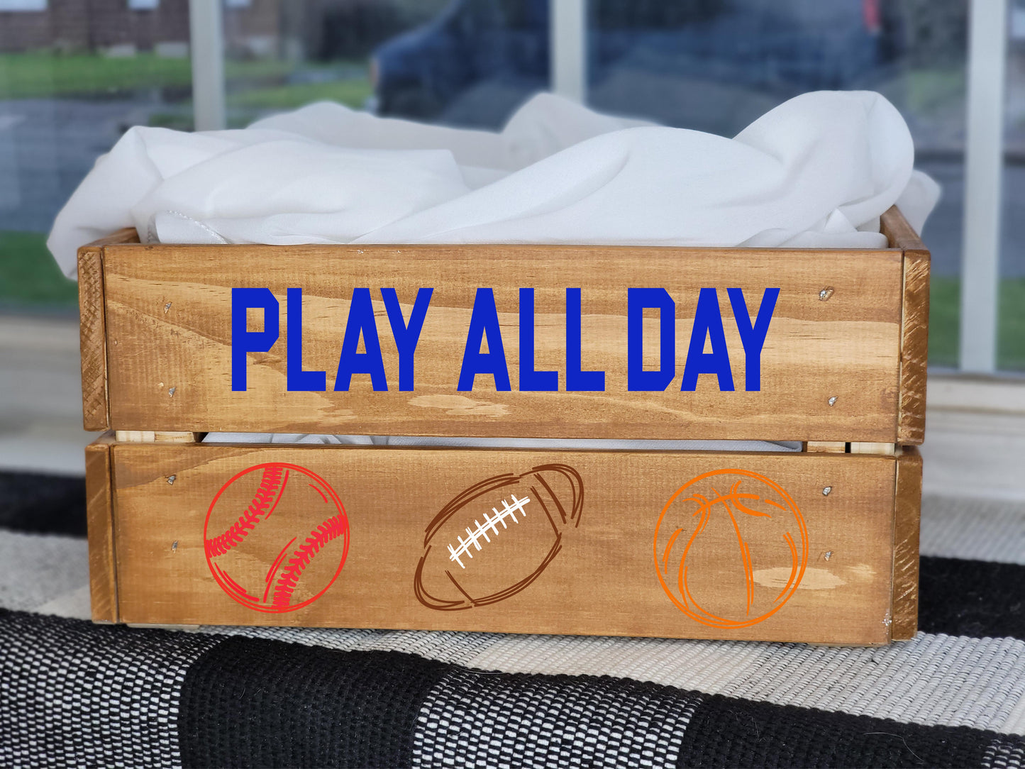 Wooden crate with 'Play All Day' text and sports icons on a grassy background