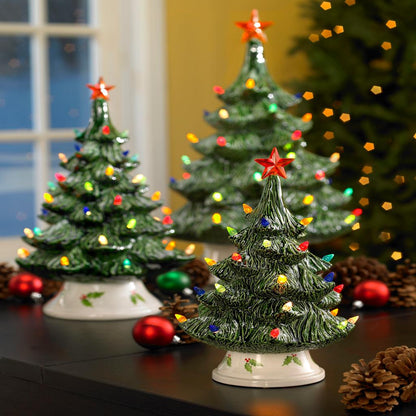 Three small ceramic Christmas trees with lights and stars on a reflective surface.
