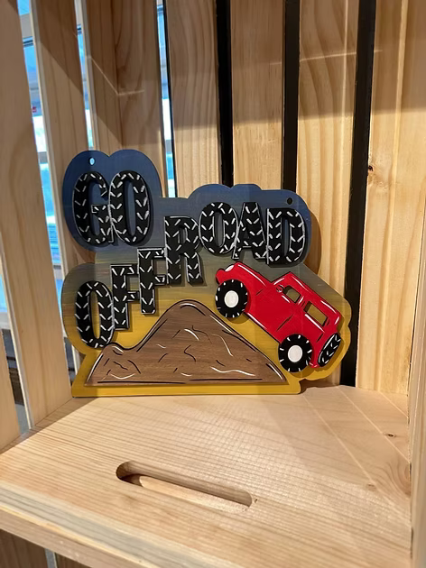 Decorative sign with 'Go Faster Off-Road' text and red car design on a wooden surface.