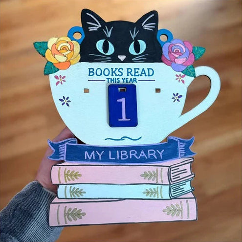Decorative reading milestone with a cat design, books, and flowers on a wooden surface.