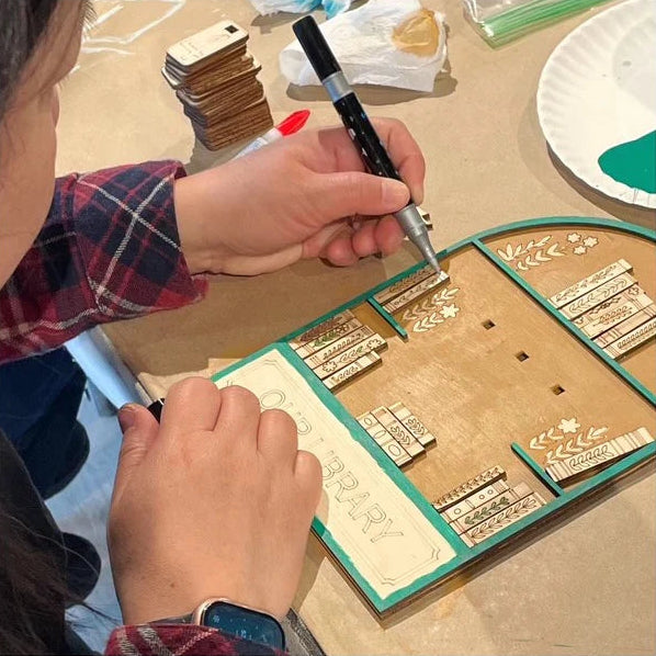 Person using a tool to work on a wooden stamp set on a table.
