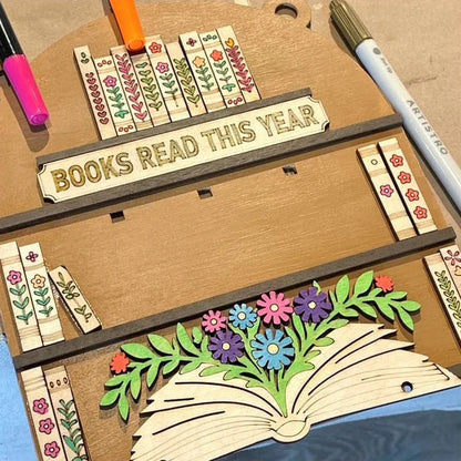 Wooden bookmark tracker with floral designs and 'Books Read This Year' text on a cardboard background.