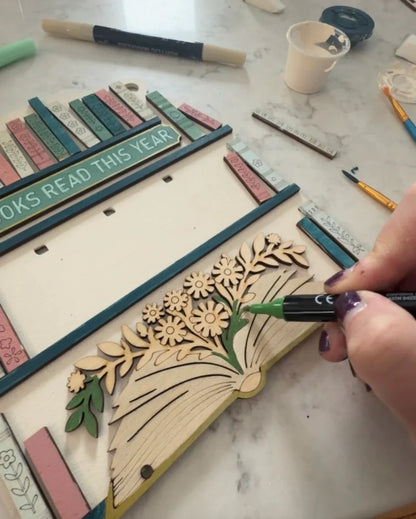 Person decorating a wooden craft with floral designs on a marble surface.