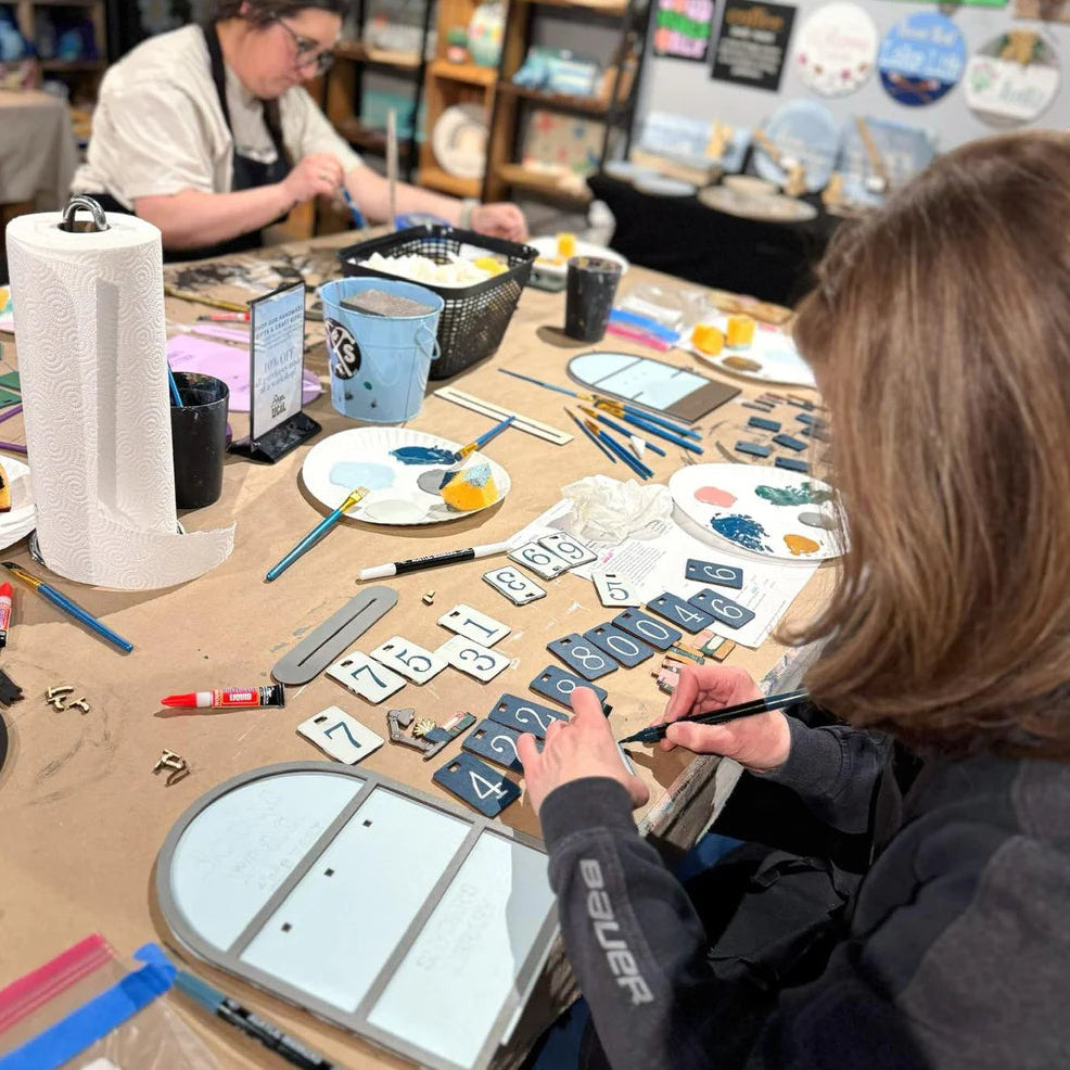 Two people working on a craft project at a table with various materials.
