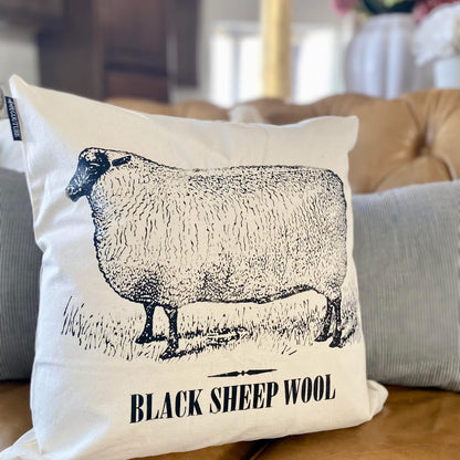 Pillow with a black sheep illustration and 'Black Sheep Wool' text on a couch.