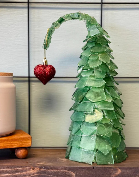 Decorative Grinch green sea glass Christmas tree with a red heart ornament on a wooden surface.
