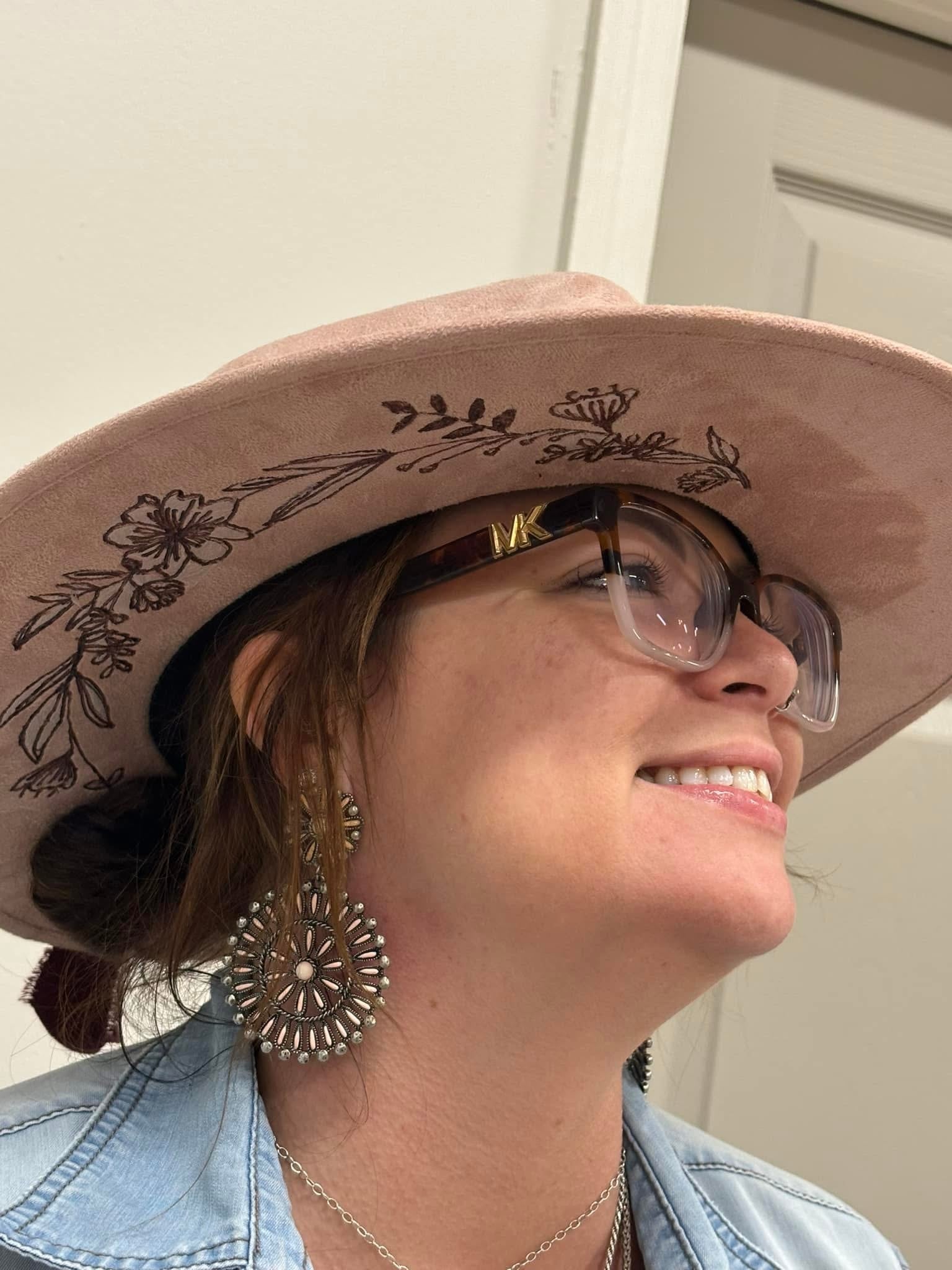 Person wearing a wide-brimmed hat with floral embroidery, glasses, and large earrings.