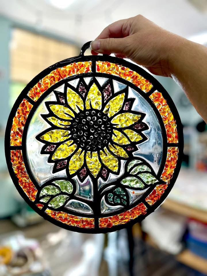 Decorative stained glass sunflower panel held by a hand in an indoor setting.