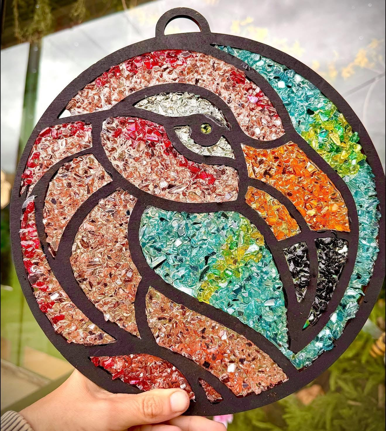 Colorful mosaic flamingo design held by a hand with a blurred natural background