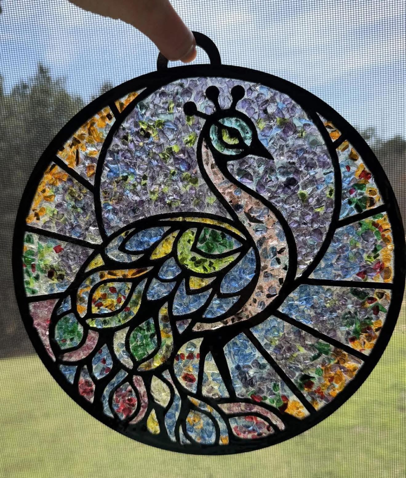 Stained glass peacock panel held against a screen