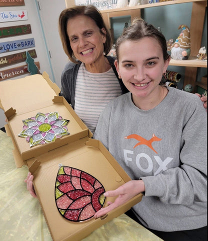 Two people holding a box with colorful mosaic art pieces.