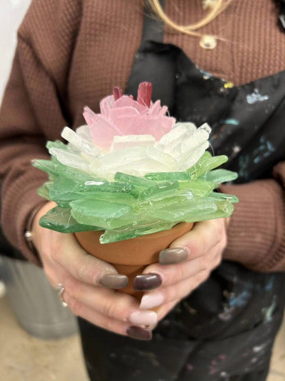 Person holding a decorative glass plant with pink and green colors.