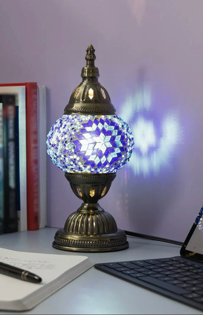 Decorative lamp with mosaic design on a desk with books and a keyboard.
