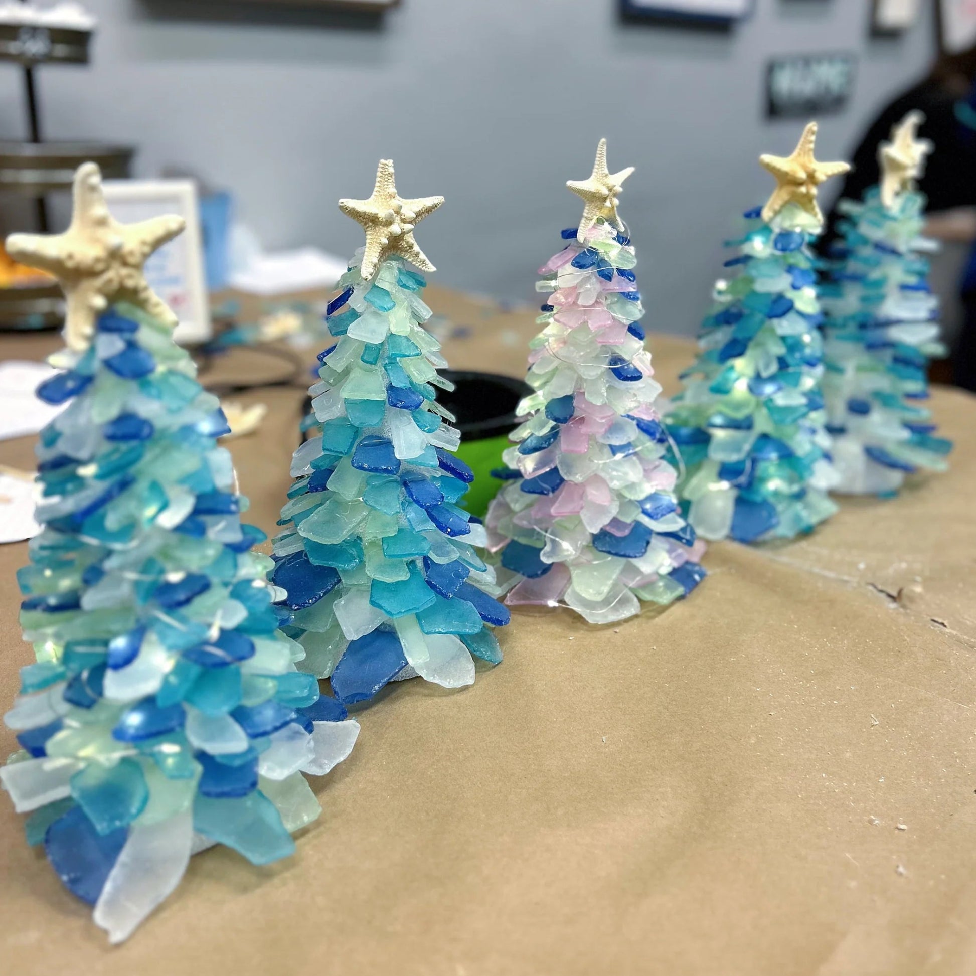 Decorative Christmas trees made from sea glass on a cardboard surface.