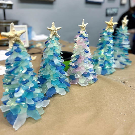 Decorative Christmas trees made from sea glass on a cardboard surface.