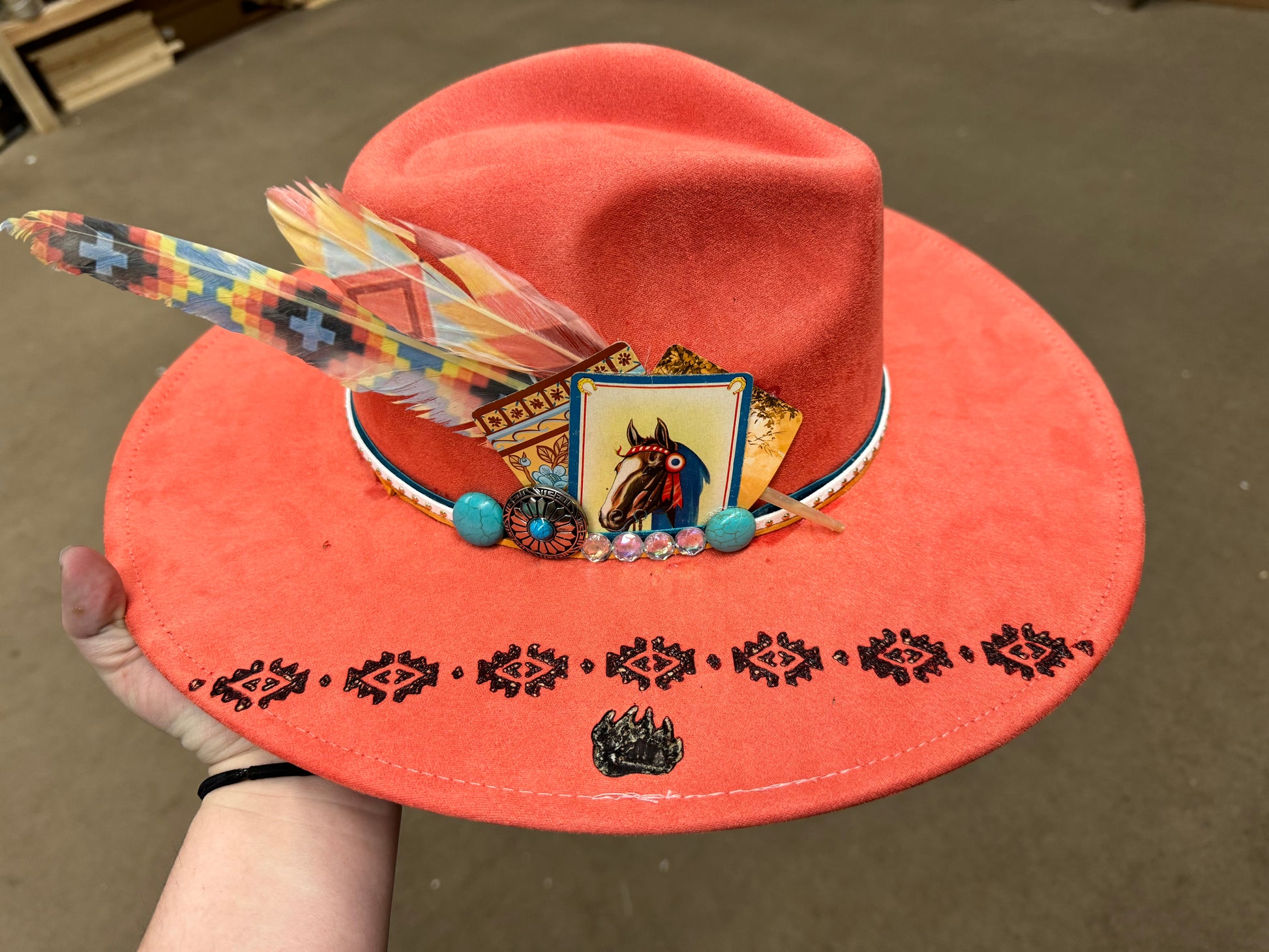 Orange hat with decorative elements held by a hand on a neutral background