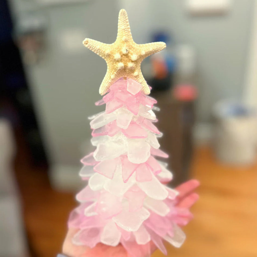 Decorative pink and white tree with a gold starfish on top, held by a hand.