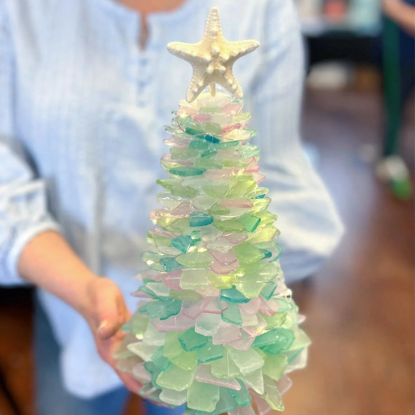 Decorative Christmas tree made of sea glass with a starfish on top, held by a person.