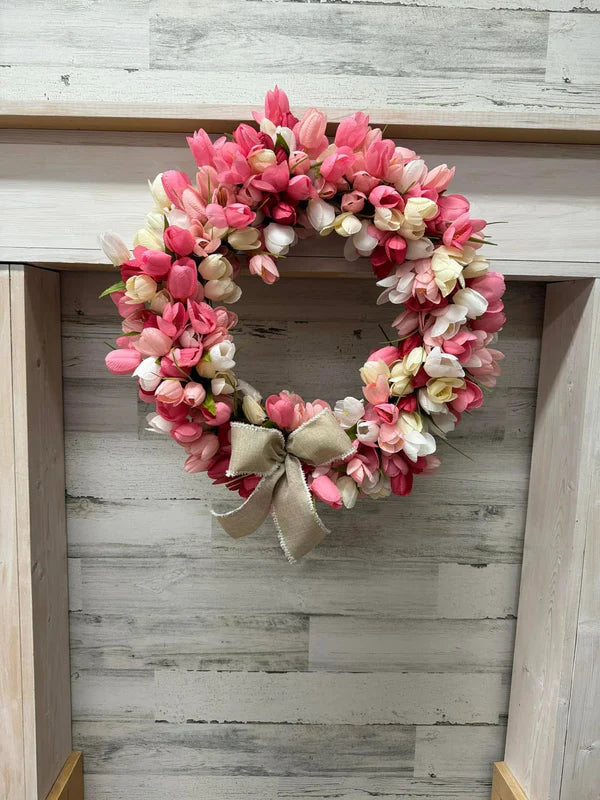 Floral wreath with pink and white flowers and a beige bow on a wooden surface.