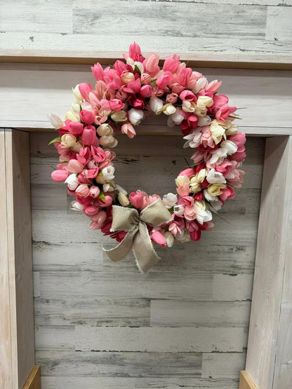 Floral wreath with pink and white flowers and a beige bow on a wooden surface.