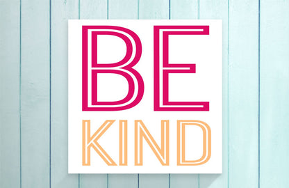 Poster with 'BE KIND' text in pink and orange on a light blue wooden background