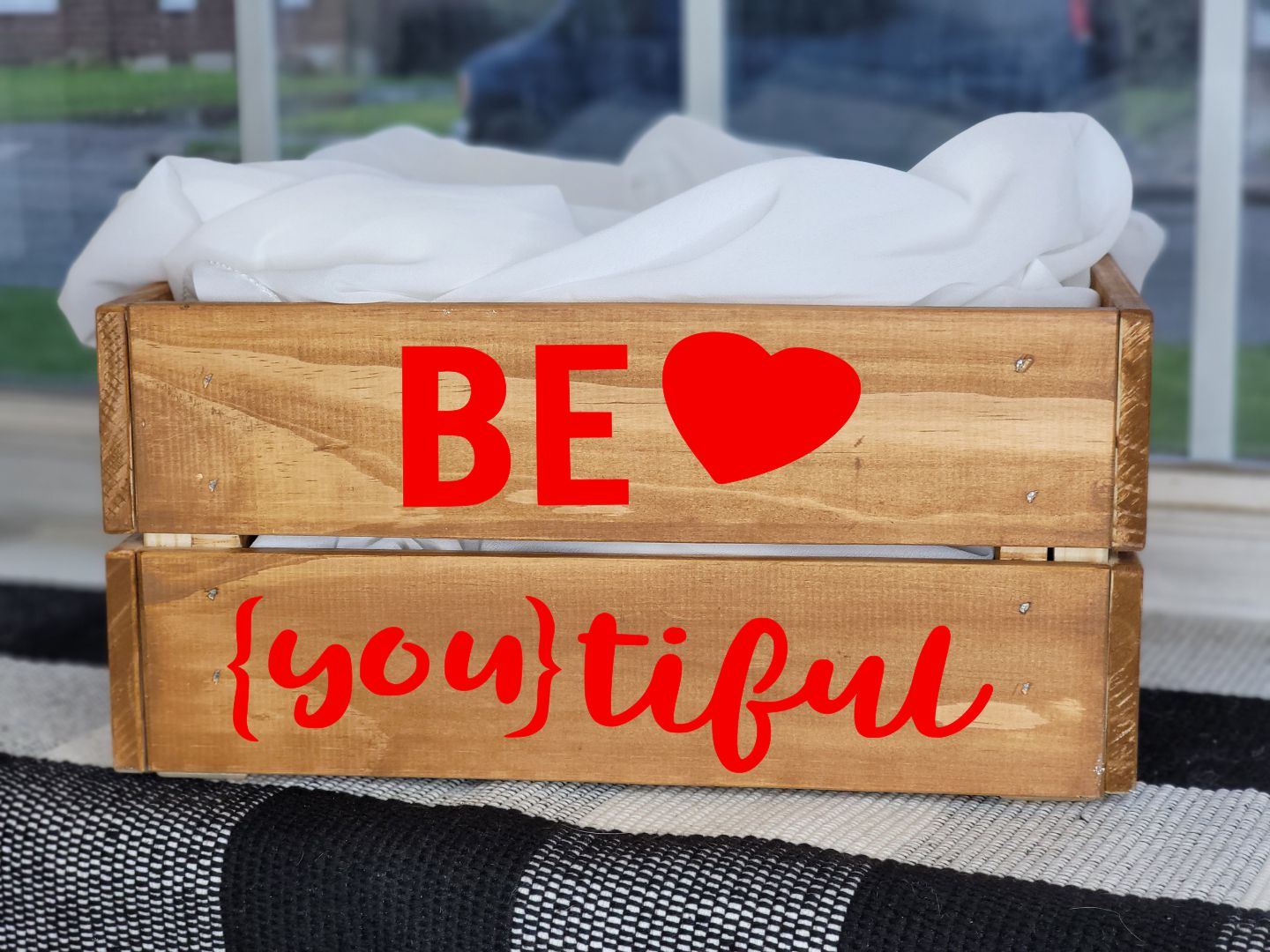 Wooden crate with 'BE ❤️ ❤️ {you}tiful' text on a blurred outdoor background