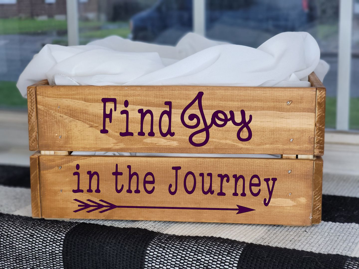 Wooden crate with 'Find Joy in the Journey' text on a black and white striped rug.